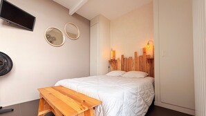 A bedroom with a bed, a wooden bench, a flat-screen TV, two wall-mounted mirrors, and a headboard with built-in lighting.