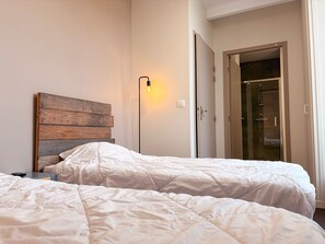 A bedroom with two beds, a wooden headboard, a bedside lamp, and a glass shower door.