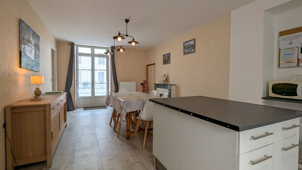 A kitchen with a dining table, chairs, a microwave, cabinets, and a window with curtains. - Charming Ground-Floor Cottage in Brenne with Enclosed Courtyard, Near Fishing and Birdwatching Spots (Neuillay-les-Bois)