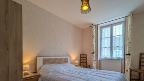 A bedroom with a large bed, a nightstand with a lamp, a chair, and a window with curtains. - Charming Ground-Floor Cottage in Brenne with Enclosed Courtyard, Near Fishing and Birdwatching Spots (Neuillay-les-Bois)