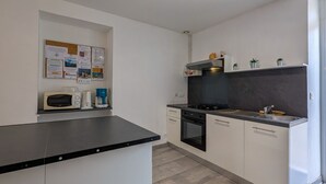 A modern kitchen with a black countertop, white cabinets, a built-in oven, and a stove. There is a microwave on the countertop, and a bulletin board with notices on the wall. - Charming Ground-Floor Cottage in Brenne with Enclosed Courtyard, Near Fishing and Birdwatching Spots (Neuillay-les-Bois)