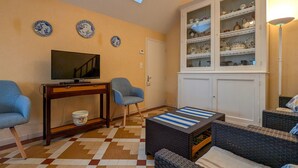 Una sala de estar con televisor, dos sillones, una mesa de centro, un aparador con vajilla y un suelo a cuadros.