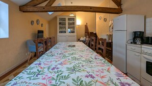 Una cocina con una mesa larga, sillas, un refrigerador y una cafetera.