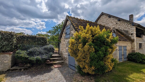 Een stenen huis met een grindpad en een kleine tuin.