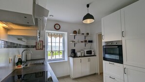 Een moderne keuken met witte kasten, een zwart aanrecht, een ingebouwde oven, een magnetron en een hangende lamp.