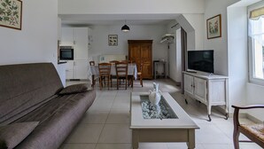 Een woonkamer met een bank, een salontafel met een decoratief object, een televisie op een kast en een eethoek met stoelen en een tafel.