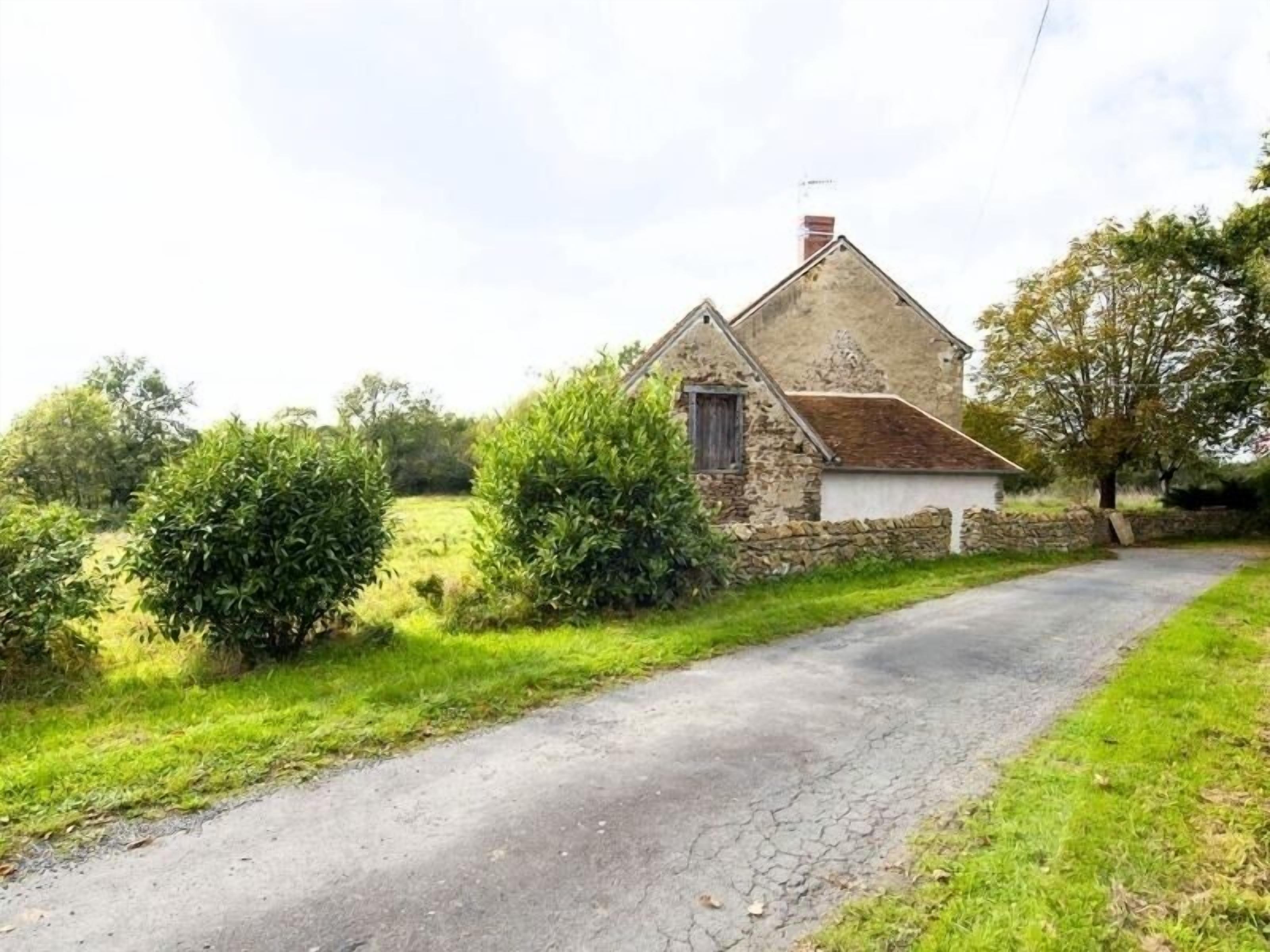 A rural stone house with a sloped roof, a small attached shed, and a narrow paved driveway.