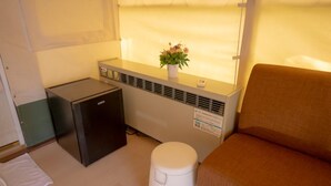 A compact room with a small kitchenette, a white trash bin, a brown sofa, and a window with a plant on the sill. - Nayang Beach (Taichung)