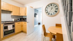 A modern kitchen with wooden cabinets, a large wall clock, and a dining area with a table and chairs. - Platform Avenues House (Hull)
