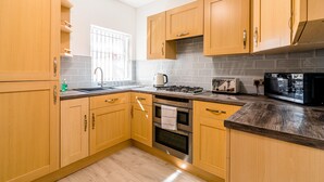 A modern kitchen with wooden cabinets, a gas stove, a microwave, and a tiled backsplash. - Platform Avenues House (Hull)