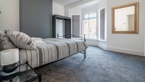 A bedroom with a bed, a nightstand, a mirror, and a window with blinds. - Platform Avenues House (Hull)