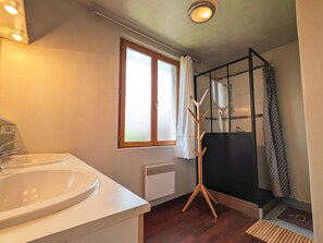 Ein Badezimmer mit Waschbecken, einem fensterbelaubten Fenster, einer Duschkabine und einem hölzernen Wäscheständer.