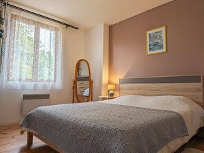 Ein Schlafzimmer mit einem Bett, einem Schminktisch, einem Spiegel, einem Nachttisch mit Lampe und einem gerahmten Bild an der Wand.