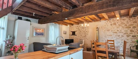A rustic kitchen with exposed wooden beams, a wooden dining table with chairs, and a white refrigerator.