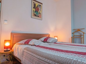 Ein ordentlich bezogenes Bett mit einem gemusterten Überwurf, einem Holz-Kopfteil, Nachttischlampen und einem an der Wand hängenden Bild.