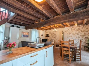 Eine rustikale Küche mit freiliegenden Holzbalken, einem weißen Kühlschrank, einem Holzessttisch mit Stühlen und einem Blumenstrauß auf der Arbeitsfläche.