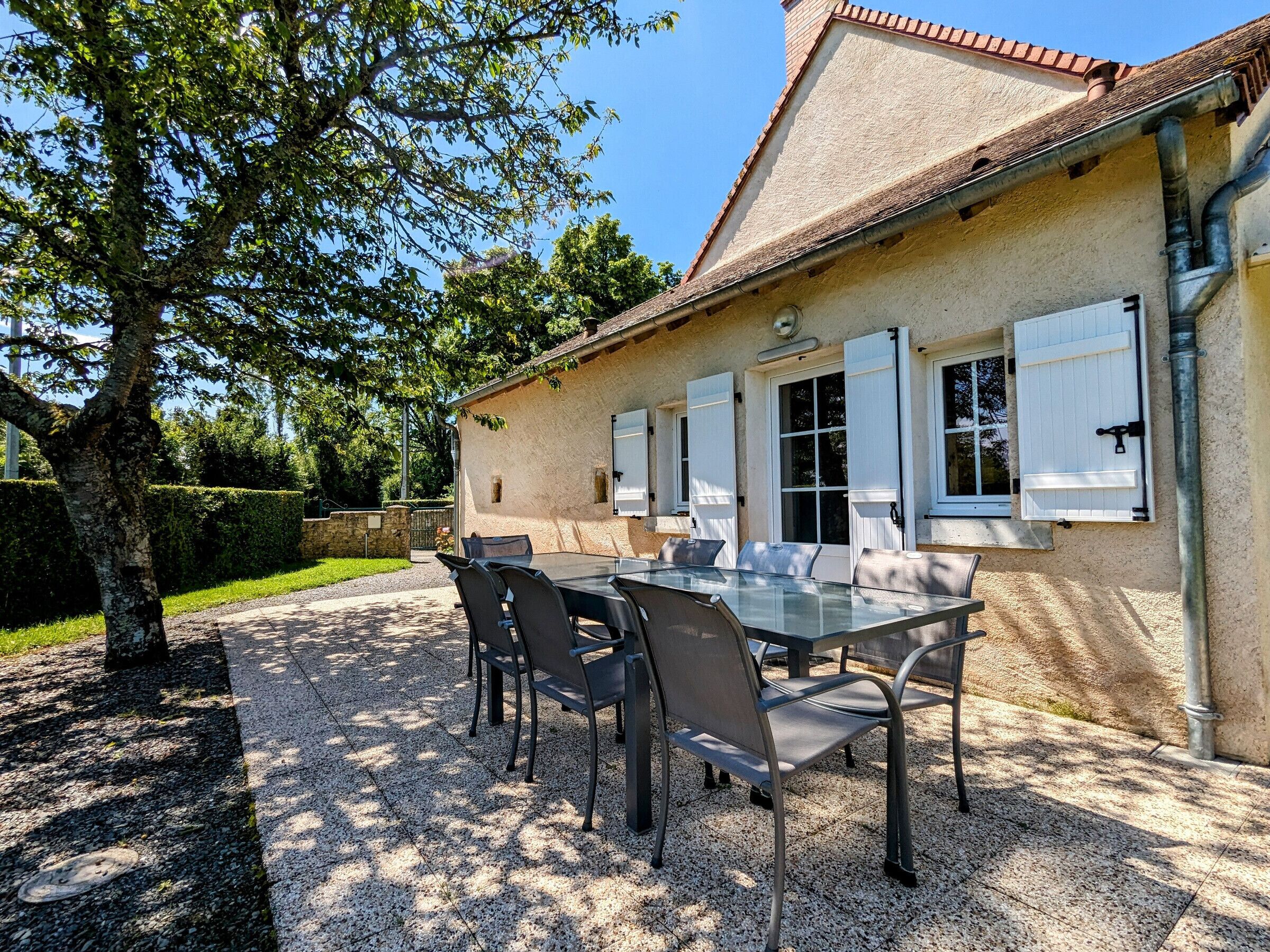 A house with a gravel patio, a dining table with chairs, and a tree.
