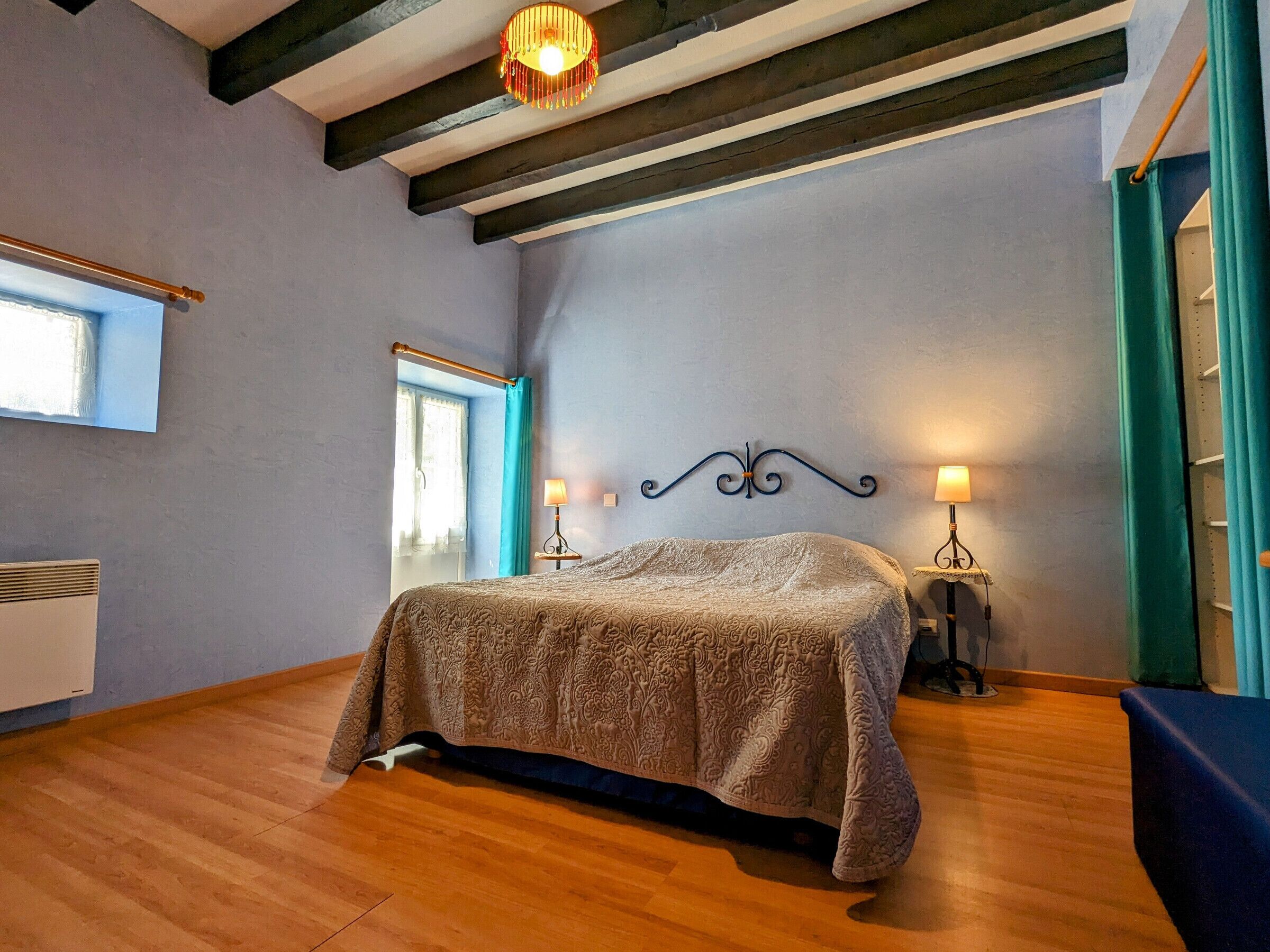 Ein Schlafzimmer mit einem Bett, zwei Nachttischlampen, einem Fenster mit Vorhängen und einem Holzboden.