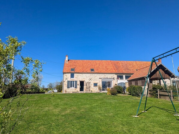 A stone house with a red roof, a grassy yard, and a swing set.