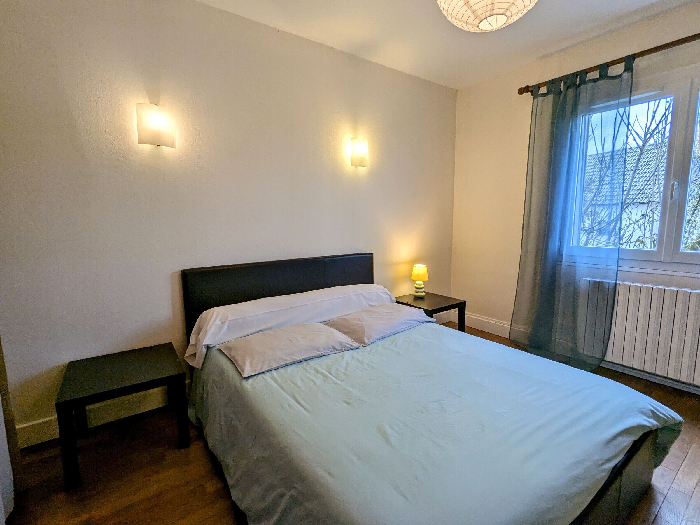 A bedroom with a bed, bedside tables, and a window with curtains.
