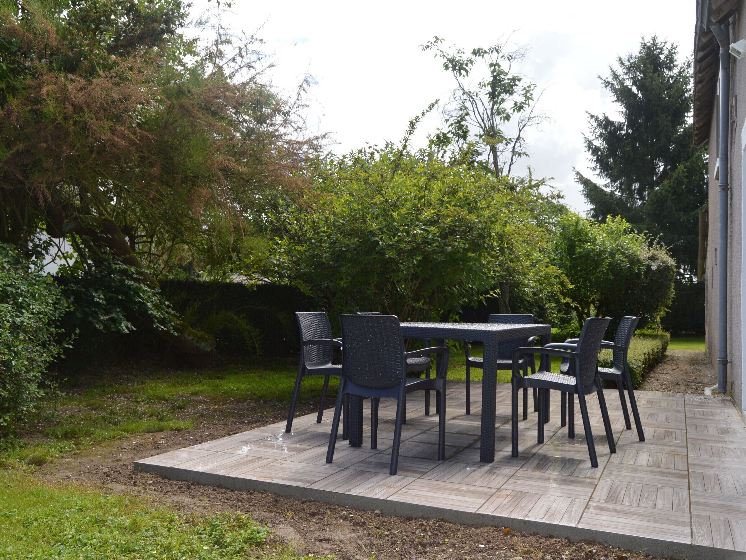 Une terrasse extérieure avec une table et des chaises, entourée de verdure et d’arbres.