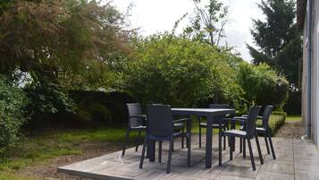 Une terrasse extérieure avec une table et des chaises, entourée de verdure et d’arbres.