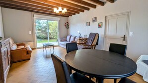 A dining area with a round table and chairs, a sofa, and a view of the outdoors through a sliding glass door. - Charming Country Cottage Near Valençay - 2 Bedrooms, Quiet Garden, Close to Loire Castles & Beauval Zoo (Poulaines)