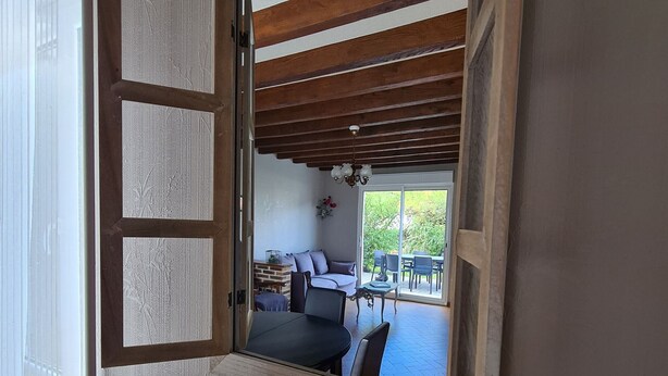 An open door leading to a room with a sofa, a small table, and a view of an outdoor patio with chairs and a table. - Charming Country Cottage Near Valençay - 2 Bedrooms, Quiet Garden, Close to Loire Castles & Beauval Zoo (Poulaines)