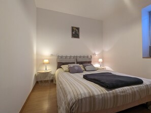 A bedroom with a bed, two bedside lamps, a small round table, and a wall-mounted picture.