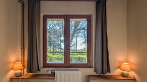 Een kamer met twee bedden, een raam met gordijnen, een radiator en twee bedlampen.