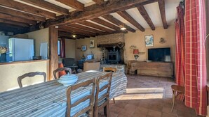 Een rustieke keuken met zichtbare houten balken, een betegelde vloer en een eethoek met een tafel en stoelen.
