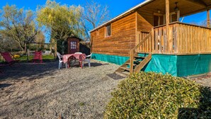 Une cabane en bois dotée d’un porche couvert, d’un sol en gravier et d’une petite table avec des chaises.