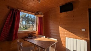 L’intérieur d’un chalet en bois comprend une table à manger, deux chaises, une fenêtre avec des rideaux rouges et un téléviseur fixé au mur.