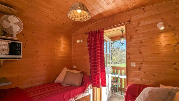 Une chambre confortable de style cabane avec deux lits simples, un plafond en bois, un petit ventilateur et une vue sur l’extérieur.