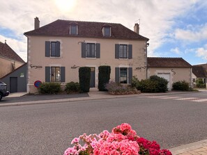 Ein zweistöckiges Gebäude mit einer symmetrischen Fassade, einem kleinen Vorgarten und blauem Himmel.