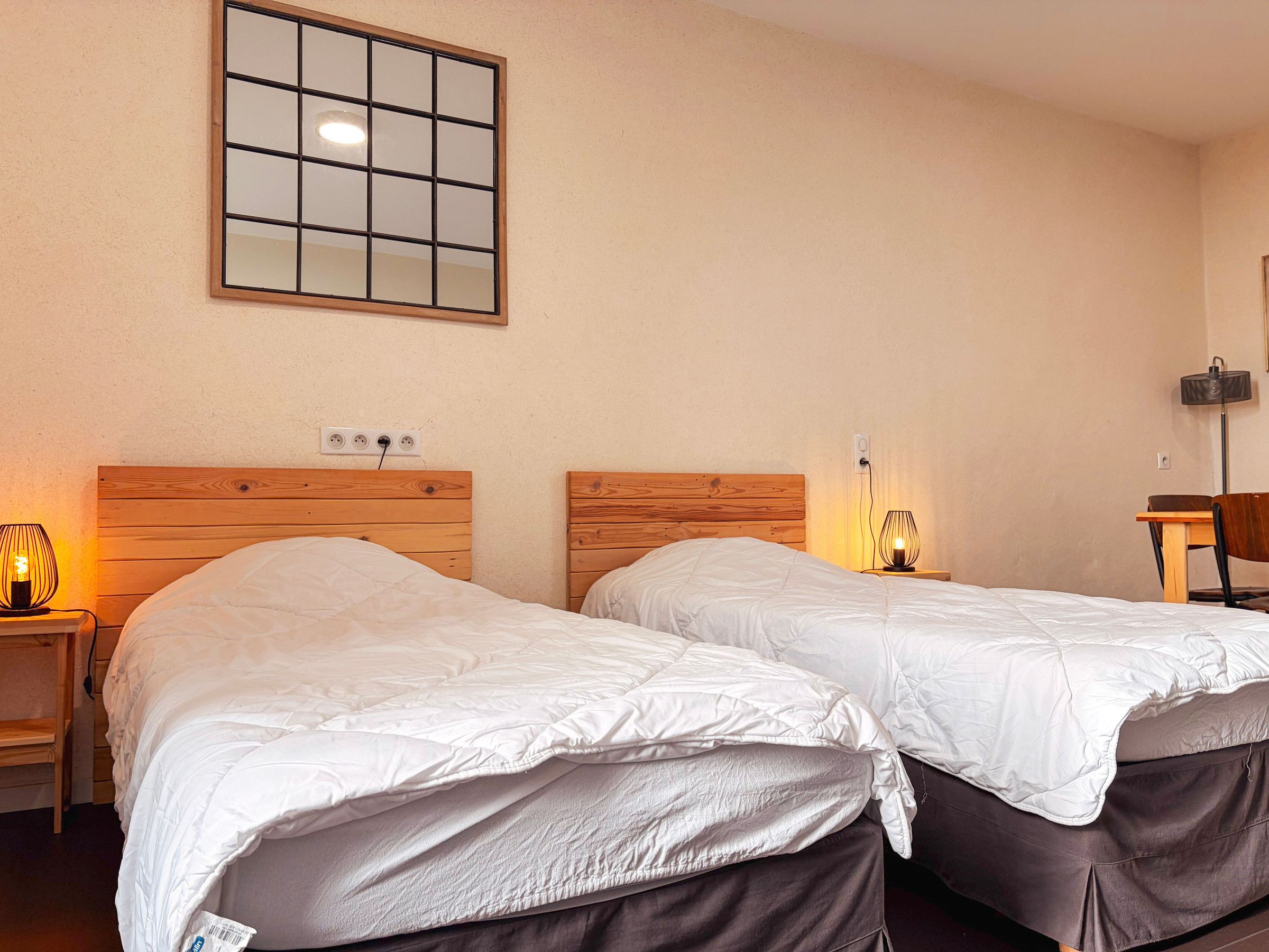 Une chambre d’hôtel avec deux lits, une table de chevet avec une lampe, une chaise et un miroir fixé au mur.