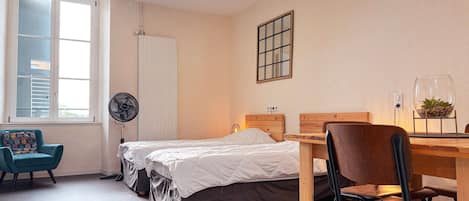 A bedroom with two beds, a desk, a chair, a fan, and a window with blinds.