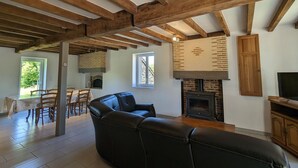 Una sala de estar amplia con vigas de madera a la vista, una chimenea, un sofá de cuero y una zona de comedor con sillas y una mesa.
