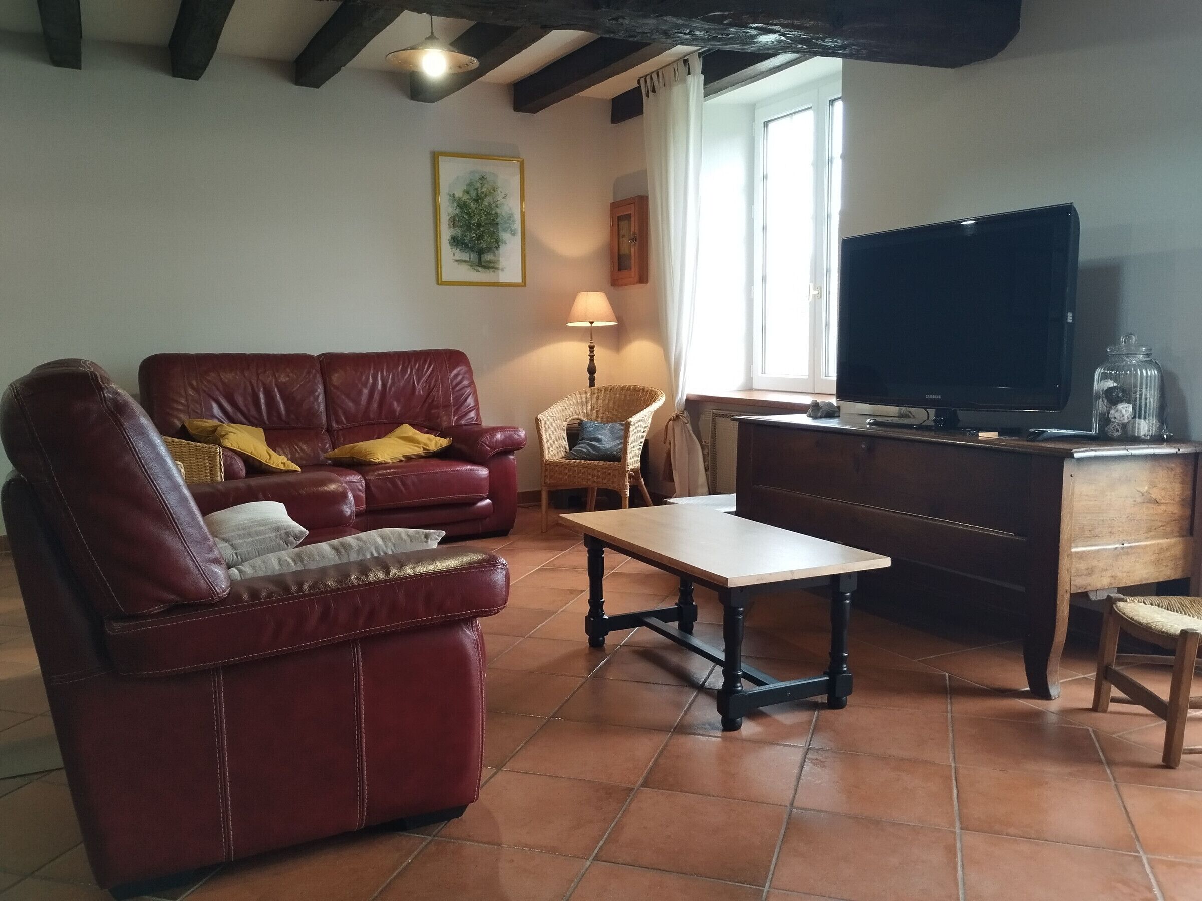 Uma sala de estar com um sofá de couro, uma mesa de centro de madeira, uma televisão e uma cadeira de vime.