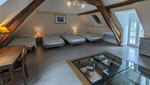 Une chambre confortable située dans les combles, avec des poutres apparentes, deux lits, une table en verre et une vue sur l’extérieur.