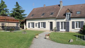 Une maison à deux étages, avec un toit en tuiles, une allée en gravier et un petit jardin agrémenté de plantes en pot.