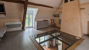 Une pièce spacieuse avec une table en verre, des poutres en bois, un meuble blanc et une chaise.