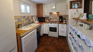 A compact kitchen with a dishwasher, stove, microwave, and a coffee maker on the countertop.