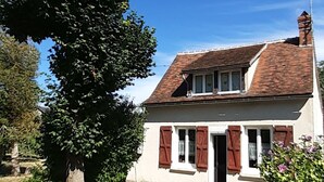 A single-story house with a sloped roof, a chimney, and a small porch with shutters.