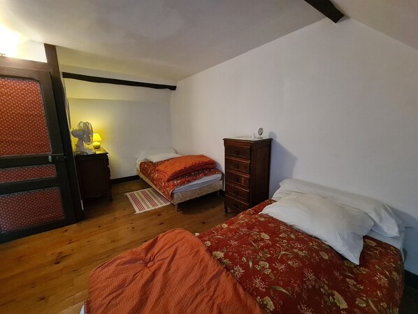 Quarto com duas camas, cômoda de madeira e mesa de cabeceira com abajur.