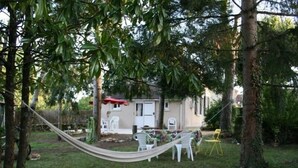 A backyard with a hammock, a small patio with chairs, and a building in the background.