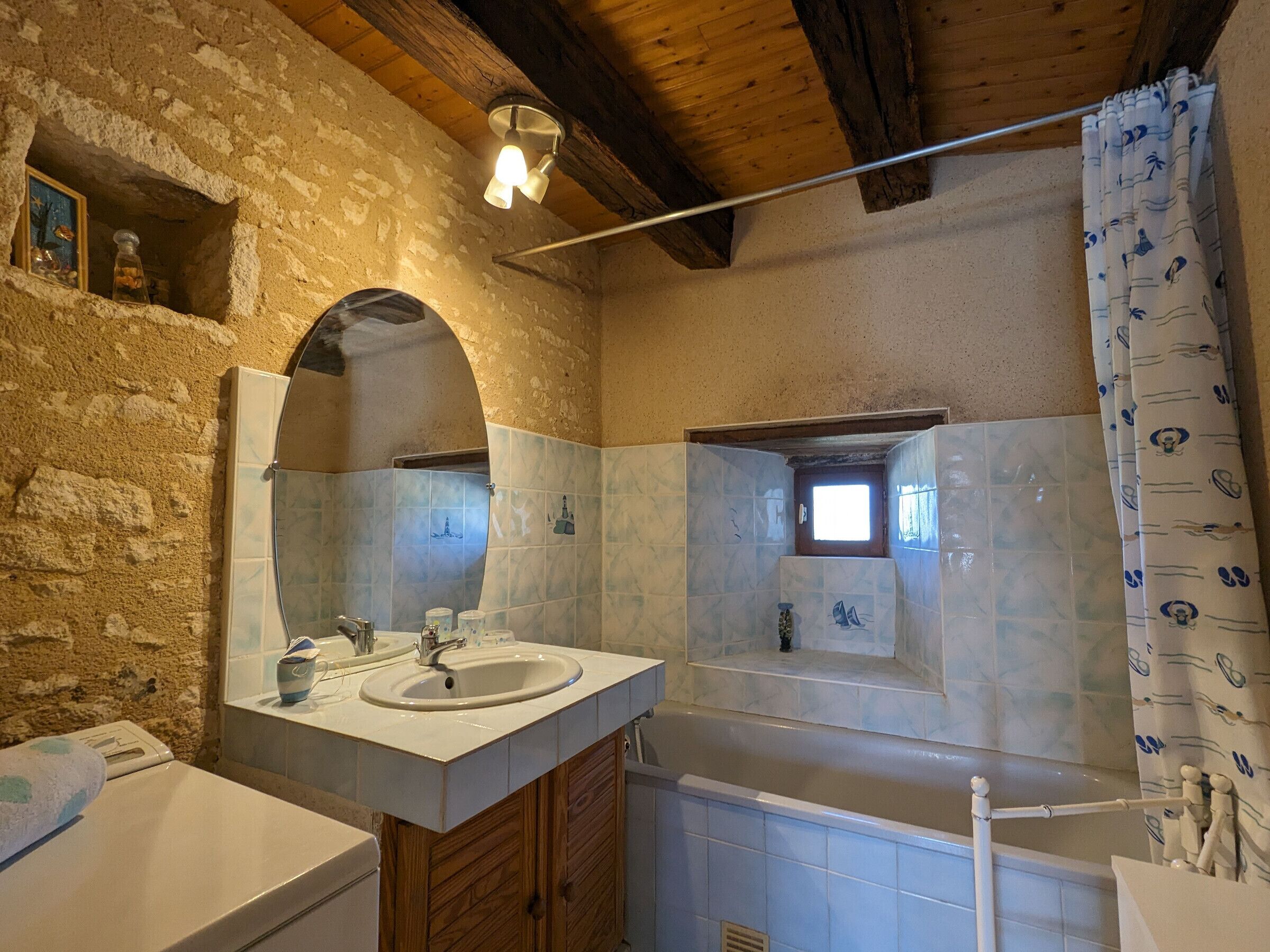 A rustic bathroom with stone walls, two sinks, wooden cabinets, and a bathtub.