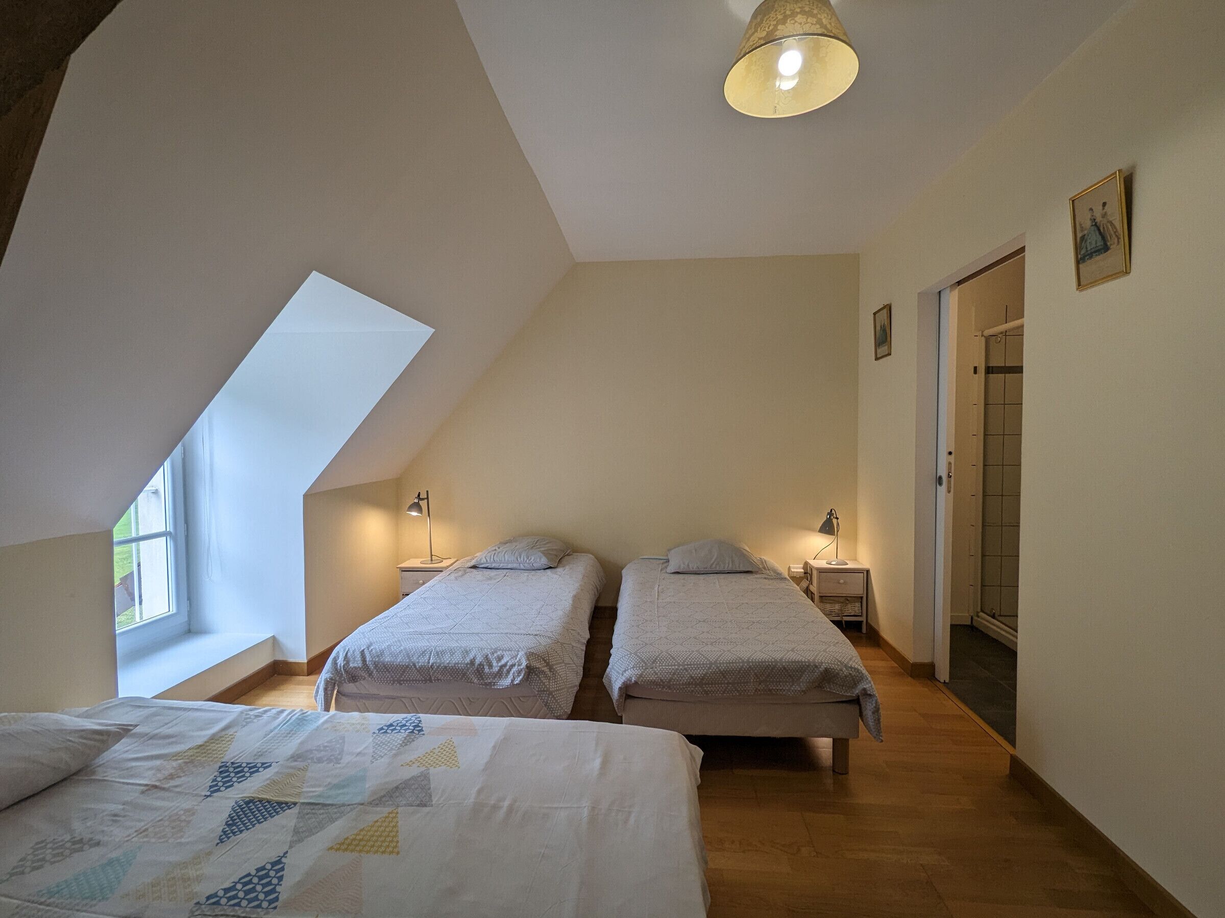 A bedroom with two single beds, a skylight, and a door leading to a bathroom.