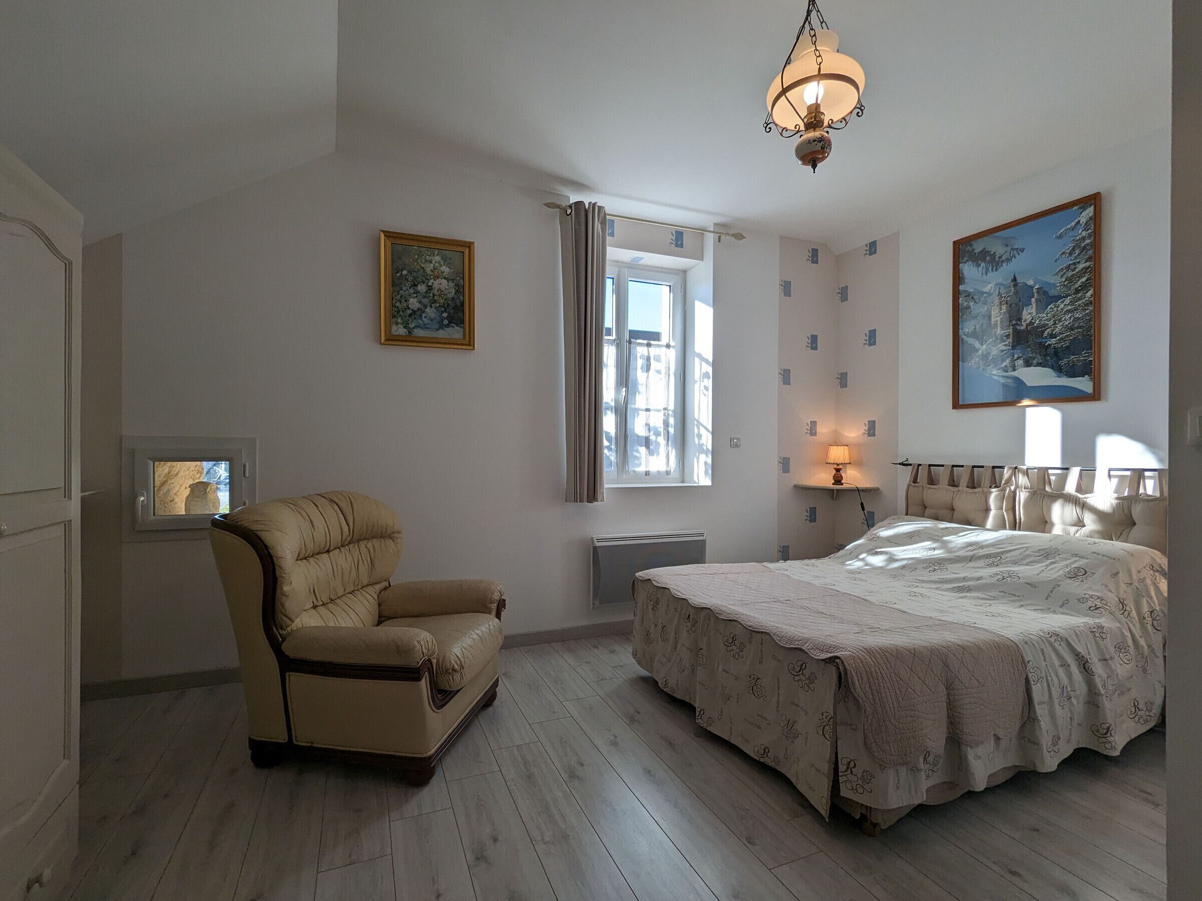 Een slaapkamer met een bed, een stoel, een raam, een schilderij en een lamp.