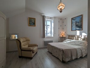 A bedroom with a bed, a chair, a window, a painting, and a lamp.